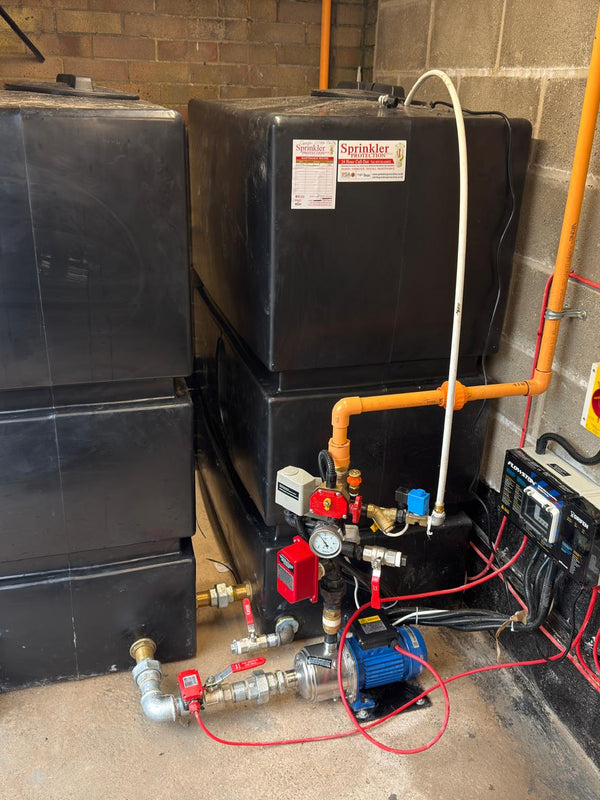 Pump room with 2 x 1200 litre fire water tanks, pipes, and electrical components against a brick wall.