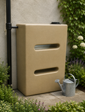650L V3 rainwater harvesting tank against a wall with a garden in the background
