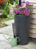 Water Butt Planter with pink flowers on a patio next to a green watering can