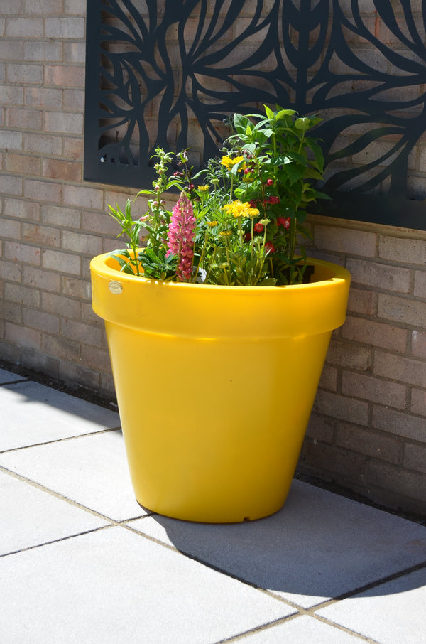 A bright yellow plastic planter pot lon a garden patio.