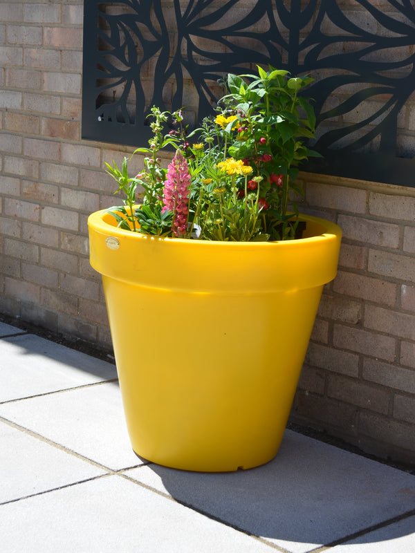 A bright yellow plastic planter pot lon a garden patio.