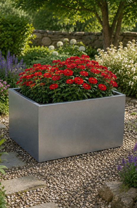 Square metal planter with red flowers in a garden setting