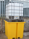 Yellow industrial spill containment IBC Bund with a white storage tank on top, against a metal fence background.