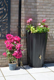 Black water butt planter with pink flowers against a tiled wall
