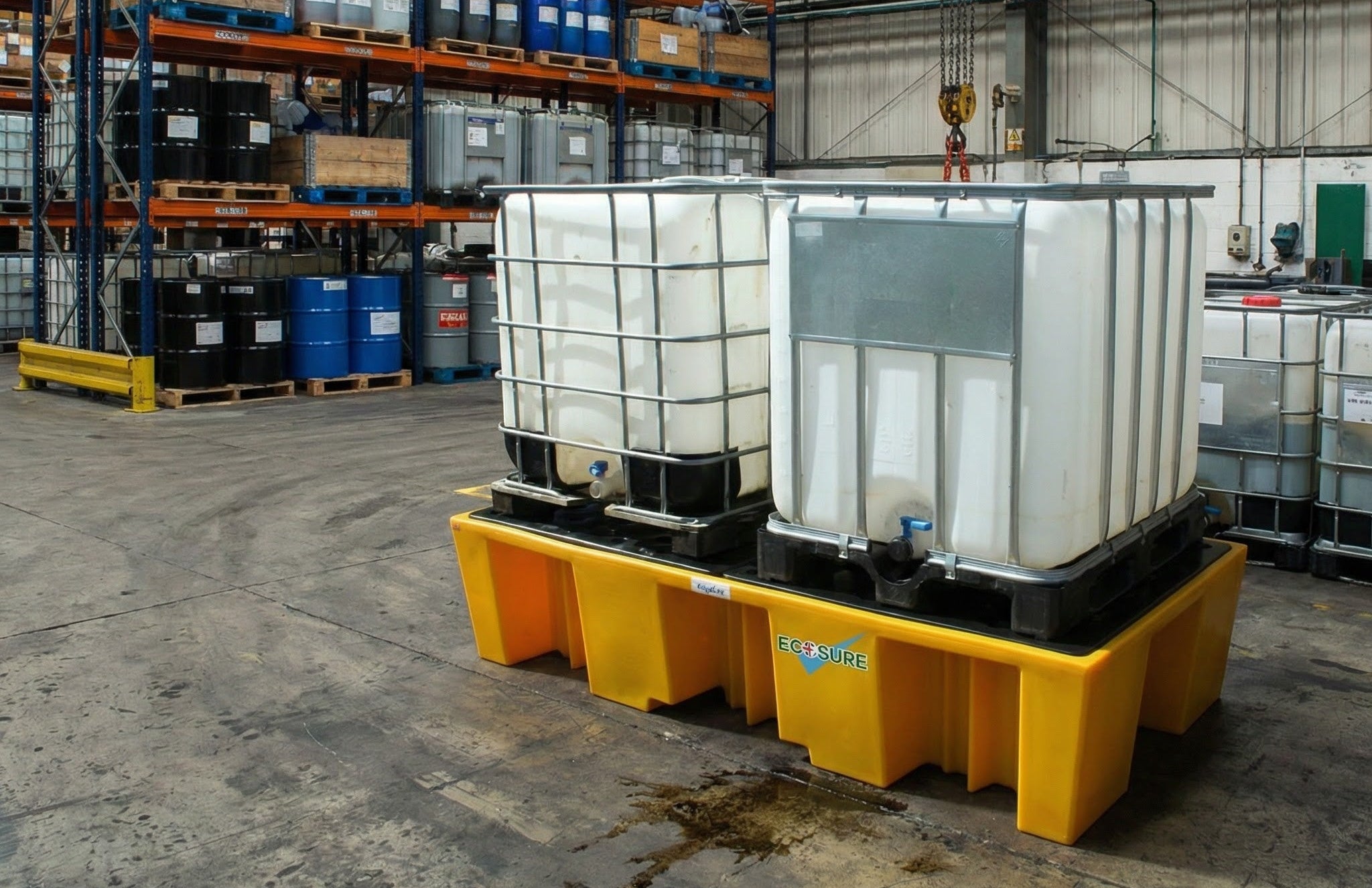 Two IBC bunds on yellow bund pallet in a warehouse setting with industrial equipment.