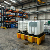 Two IBC bunds on yellow bund pallet in a warehouse setting with industrial equipment.