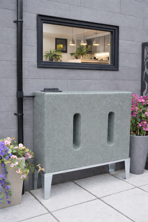 Modern 500 litre water butt with decorative plants against a gray tiled wall.
