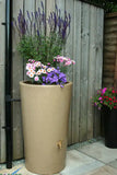 Tall cylindrical beige planter with flowers against a wooden fence